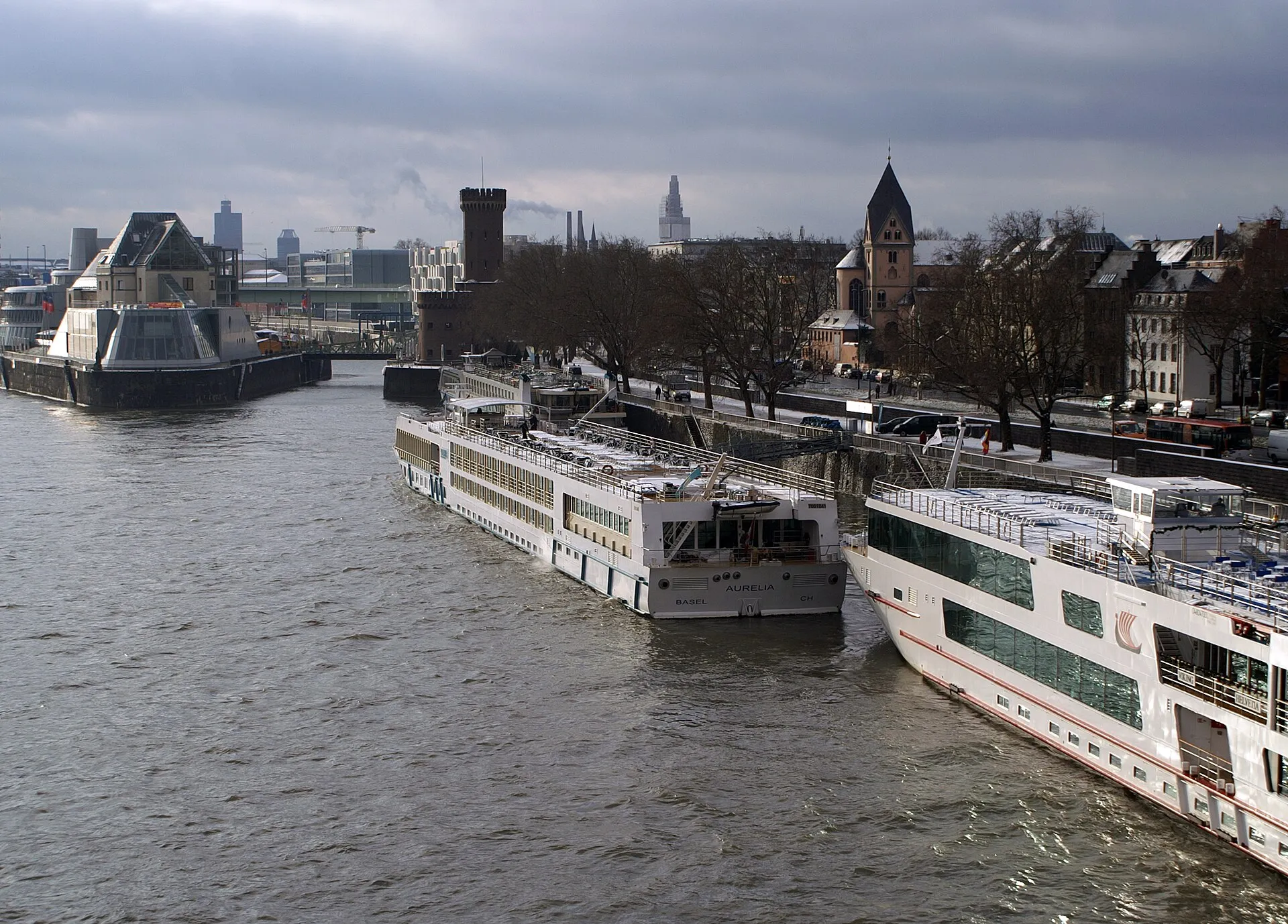 Die MS Aurelia am Anleger Köln, davor MS Swiss Gloria und dahinter MS Viking Helvetia. Im Hintergrund das Imhoff-Schokoladenmuseum, die Kölner Drehbrücke und de