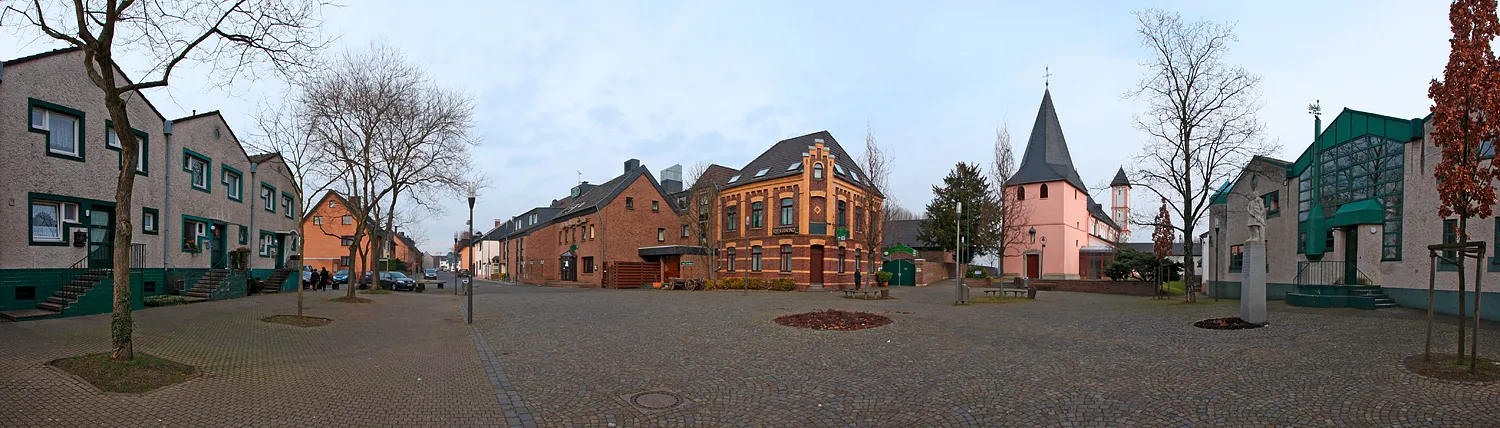 Köln-Rheinkassel Dorfplatz, Mitte St.-Amandus-Kirche, rechts und Links Teile der Amandus-Siedlung von Gottfried Böhm